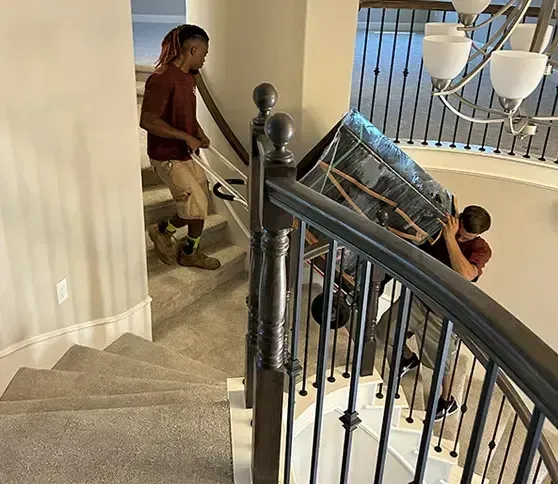 Two men are carrying a refrigerator down a set of stairs.