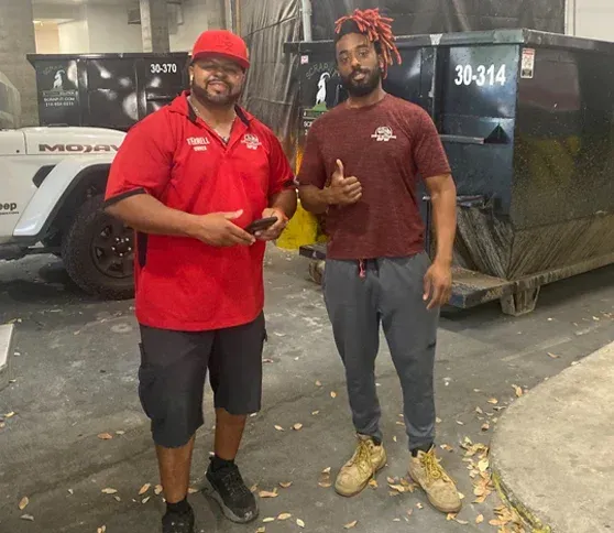 Two men are standing next to each other in front of a dumpster that says 30-314