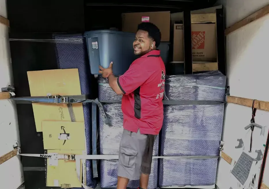 A man in a red shirt is carrying a blue bin into a moving truck.