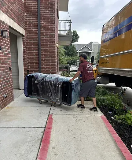A man is pushing a couch on a dolly down a sidewalk next to a truck.