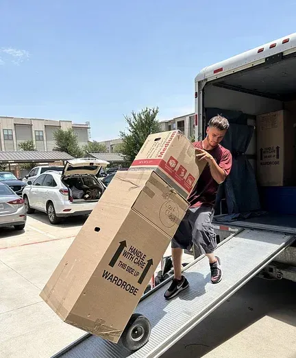 A man is pushing a large cardboard box on a dolly into a truck.