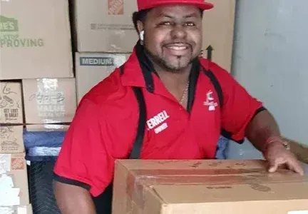 A man in a red shirt and hat is holding a box.