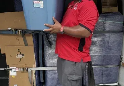 A man in a red shirt is carrying a blue container.