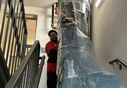 A man is carrying a large piece of furniture up a set of stairs.