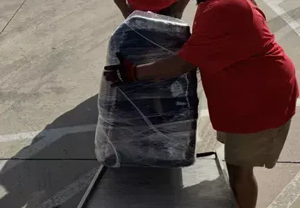 A man in a red shirt is carrying a large bag wrapped in plastic.