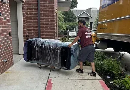 A man is carrying a large piece of furniture on a dolly.