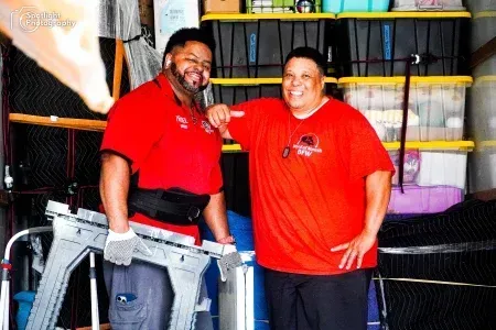 Two men in red shirts are standing next to each other in a garage.