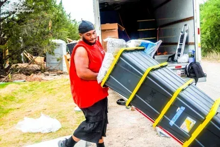 A man in a red shirt is carrying a large black box.