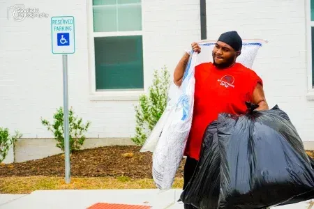 A man in a red shirt is carrying a large bag of trash.