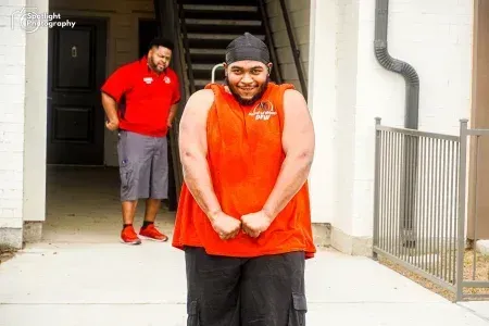 A man in a red tank top is standing in front of a building.