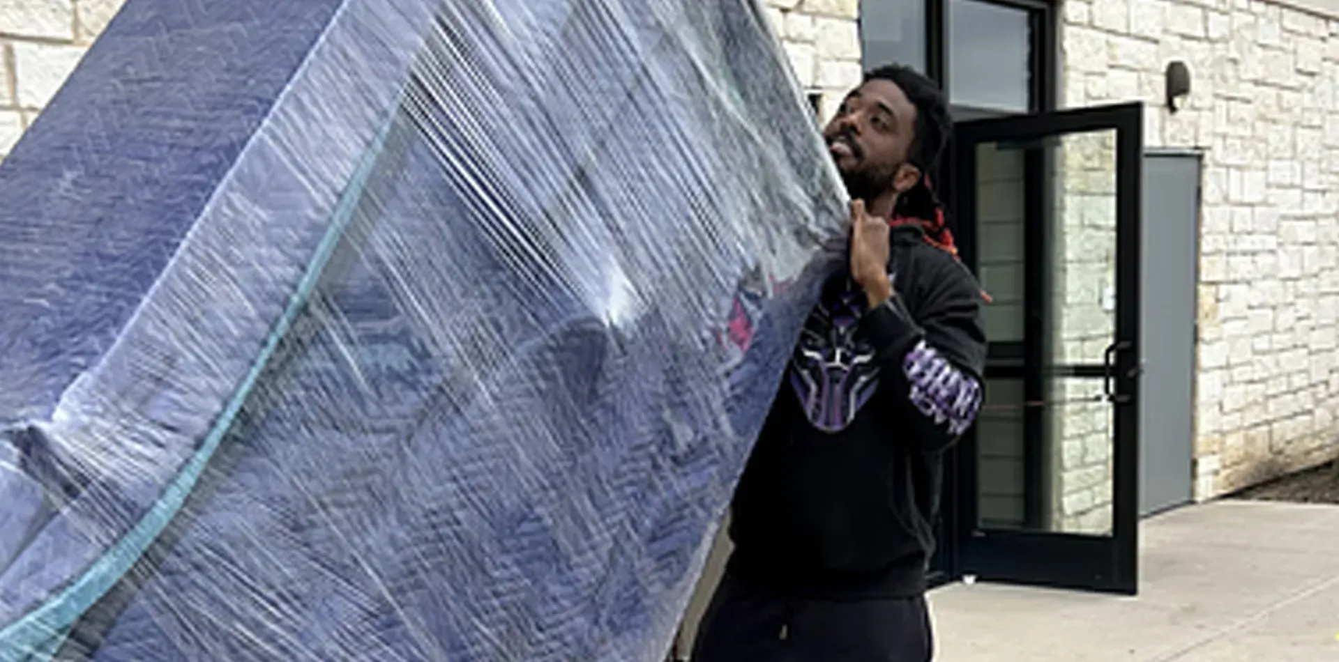 A man is carrying a large mattress on his back.