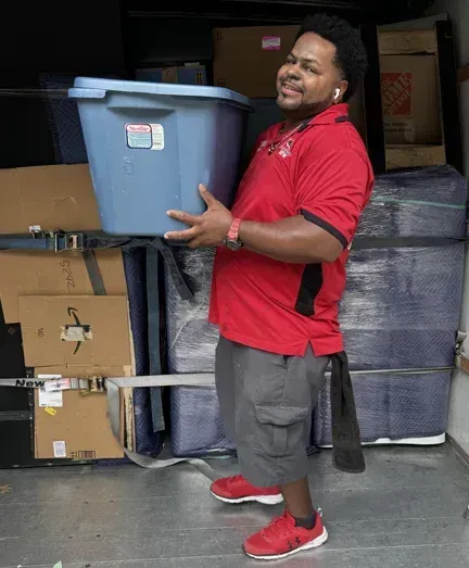 A man in a red shirt is carrying a blue bin