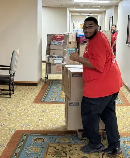 A man in a red shirt is pushing boxes in a hallway.