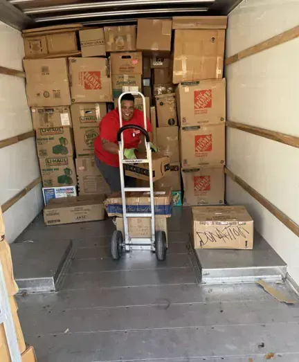 A man is pushing a dolly in a truck filled with boxes.