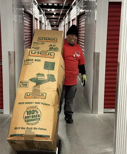 A man is pushing a large cardboard box down a hallway.