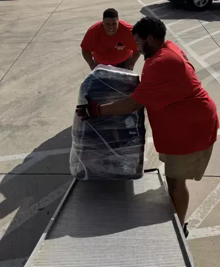 A man in a red shirt is pushing a suitcase on a ramp.