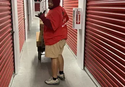A man in a red shirt is pushing a wheelbarrow down a hallway.
