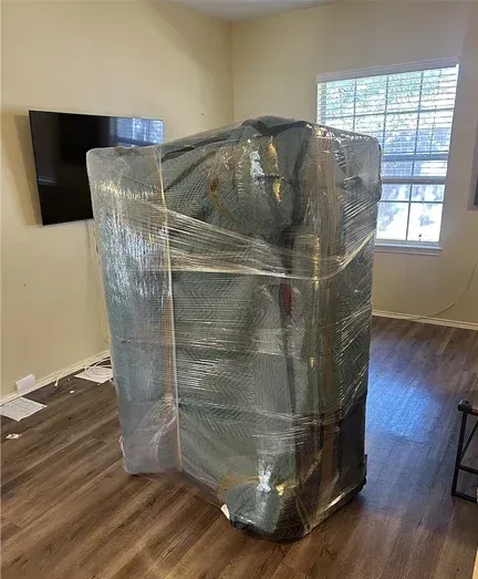 A large piece of furniture is wrapped in plastic in a living room.