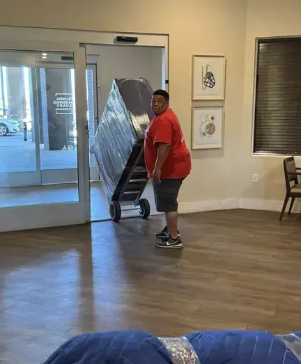 A man is pushing a large piece of furniture on a dolly in a room.