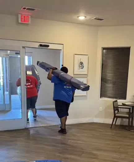 A man in a blue shirt is carrying a large piece of carpet