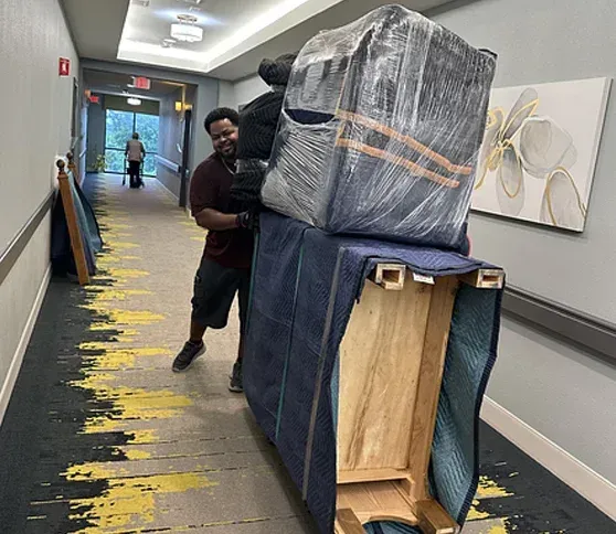 A man is carrying a large piece of furniture down a hallway.