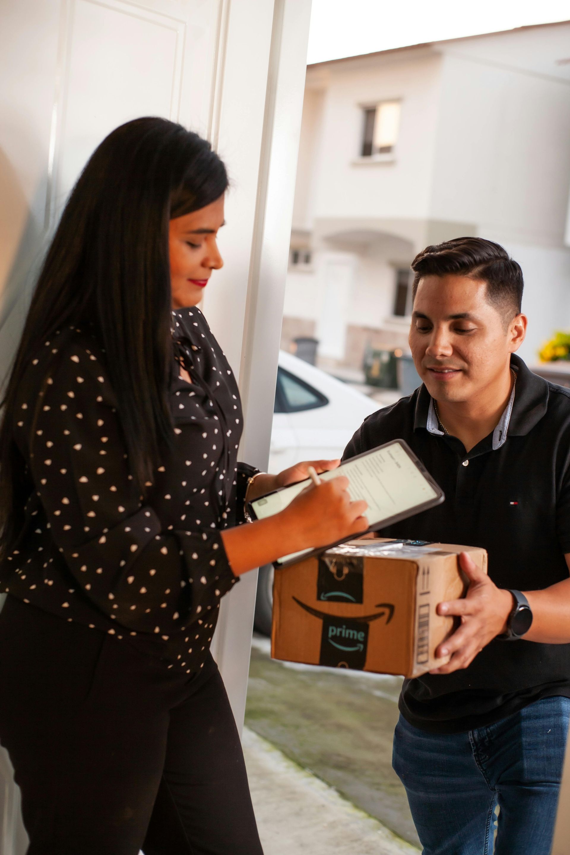Woman signing for Amazon package from delivery person at a door.
