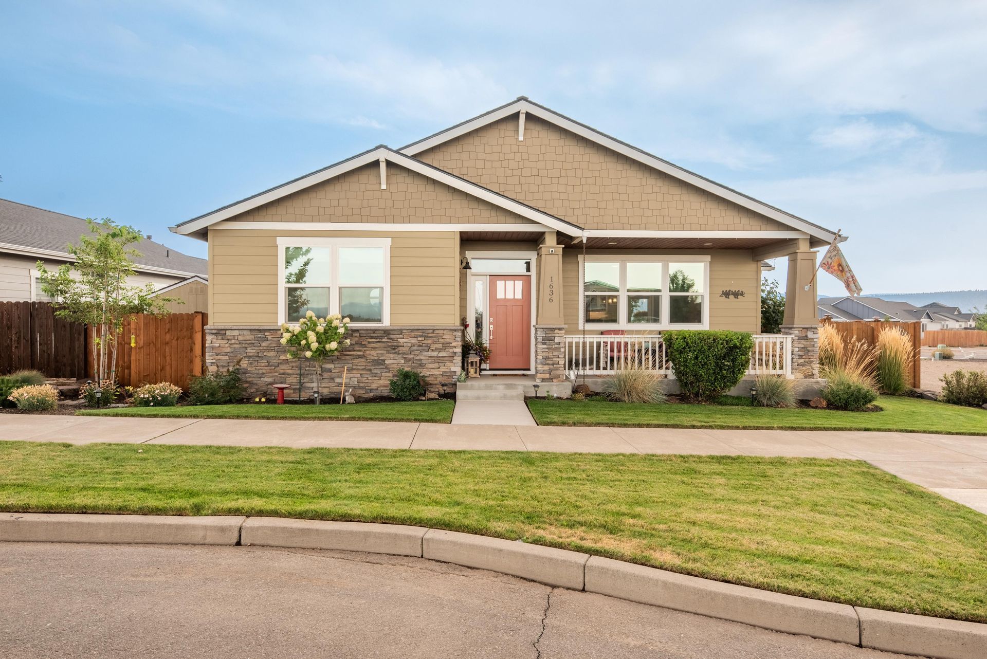 Single-story house with beige siding, stone facade, covered porch, and a reddish door under a blue sky.