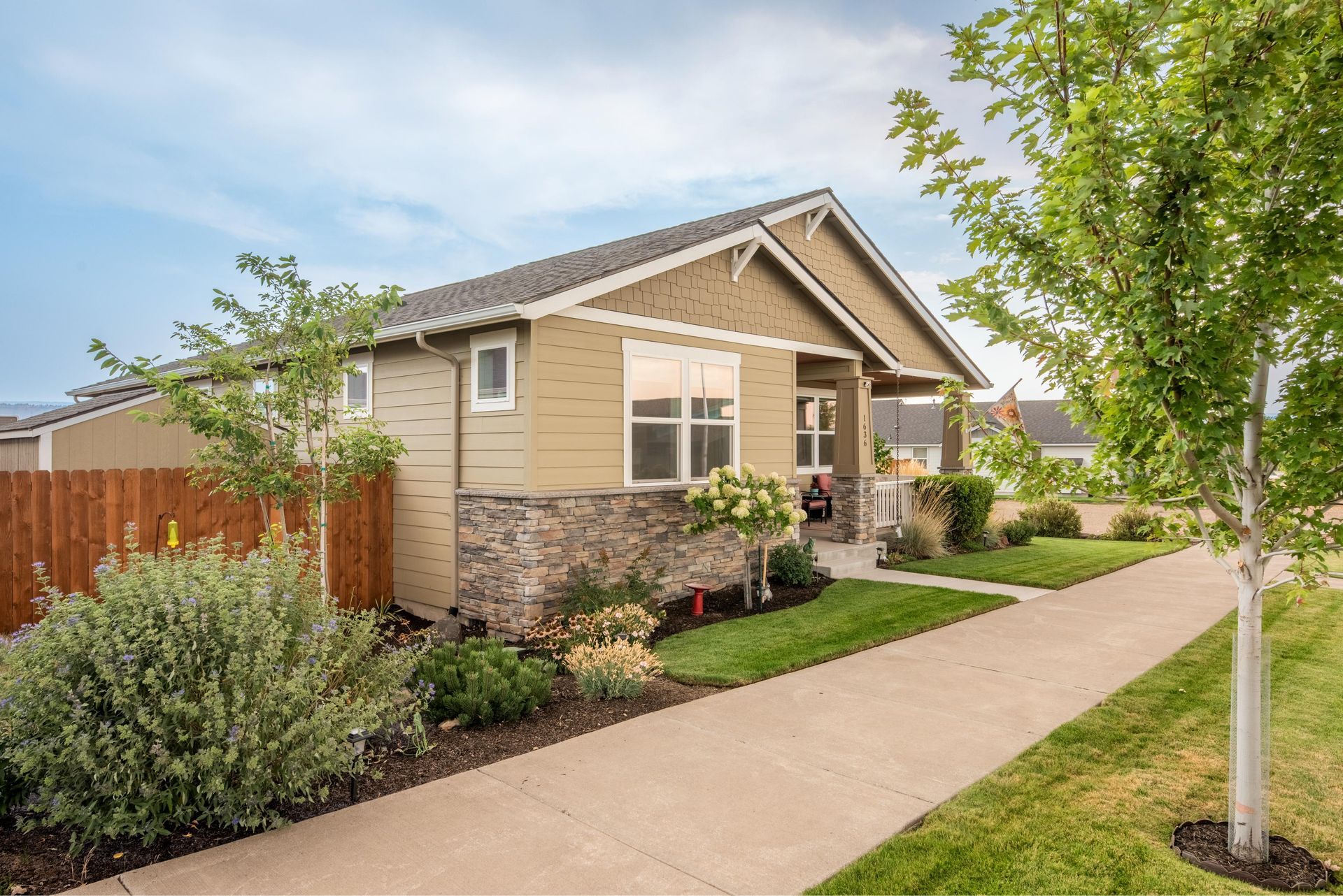 A tan single-story home with stone siding, a wooden fence, and a sidewalk leading to the entrance on a sunny day.