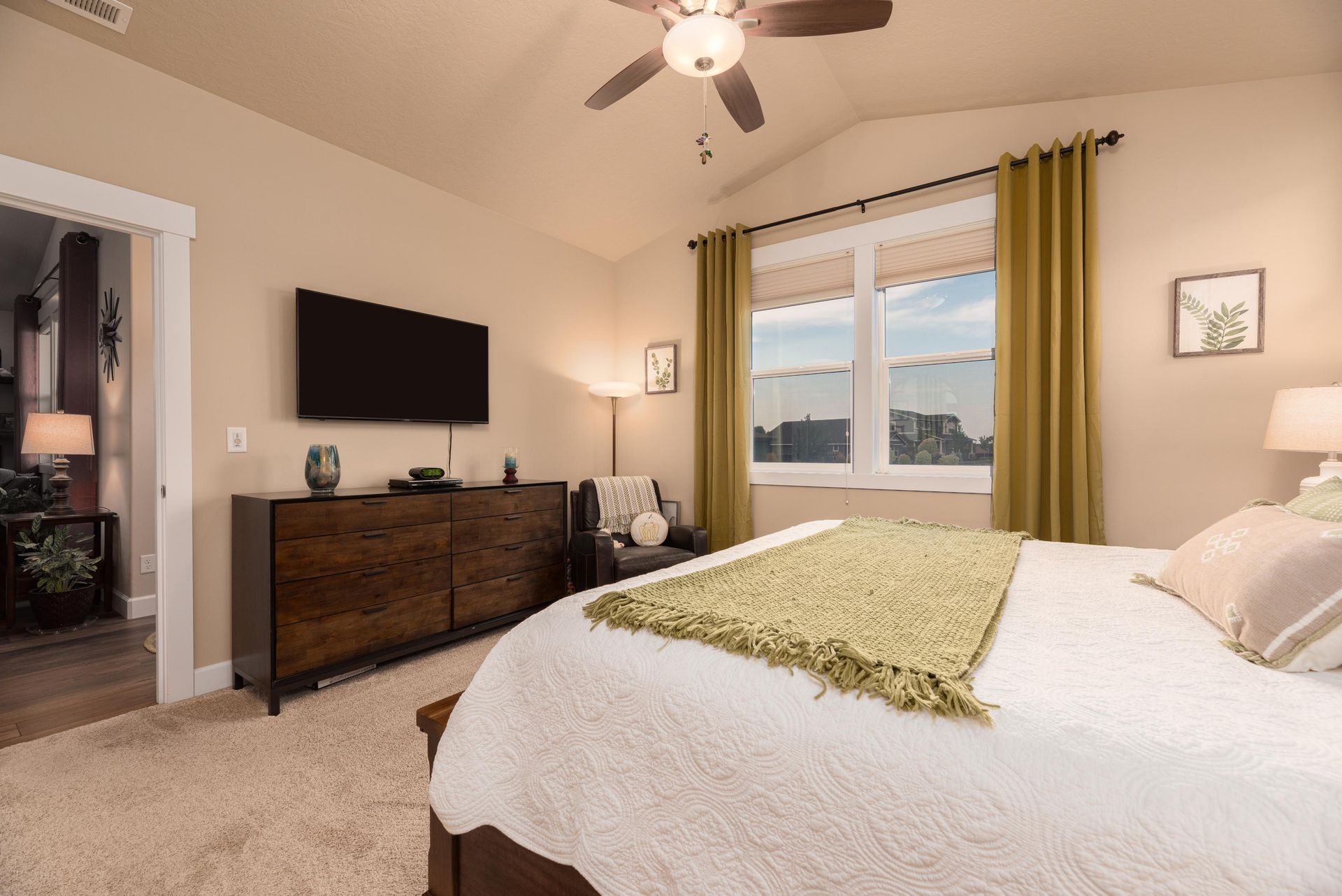 A bedroom featuring a bed with a textured green throw, a dark wood dresser, a TV, and a window with green curtains.