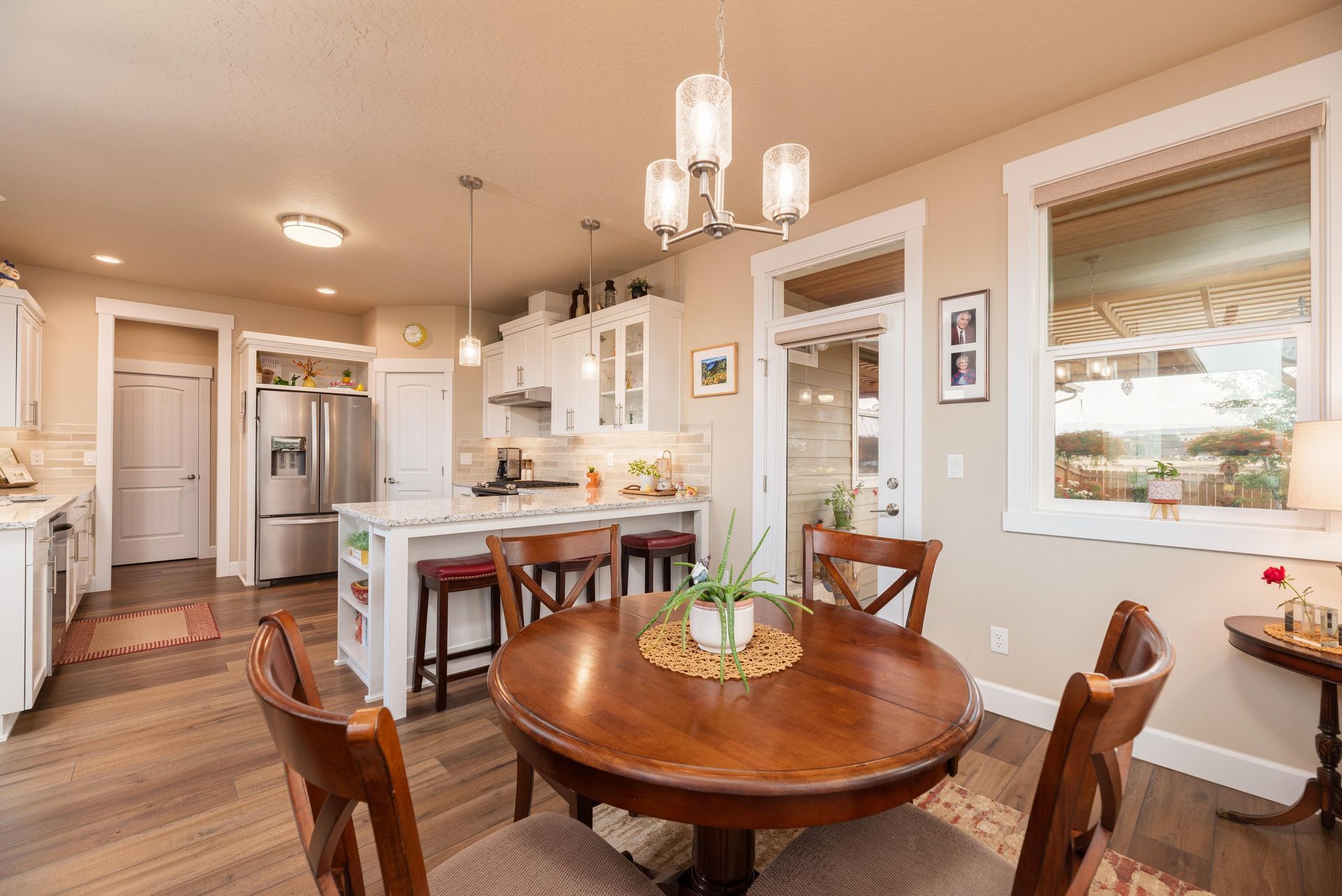 A bright, open-concept kitchen and dining area with a round wooden table, white cabinetry, and a large window.