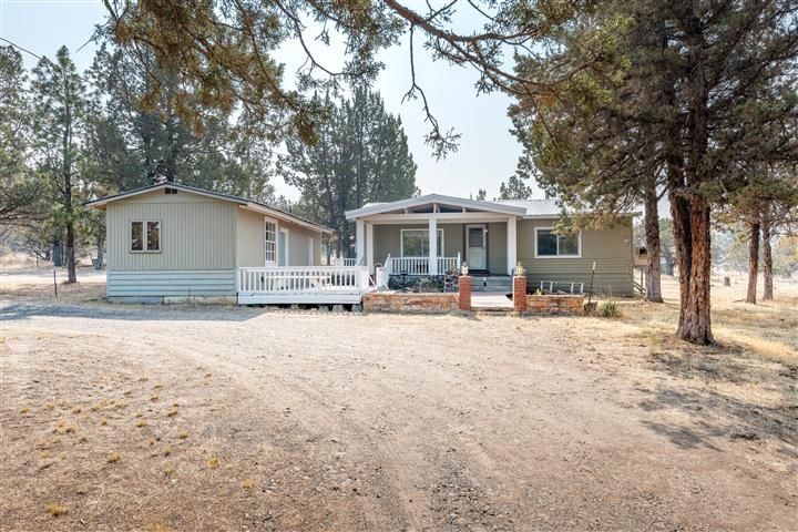 A mobile home with a large porch is surrounded by trees.