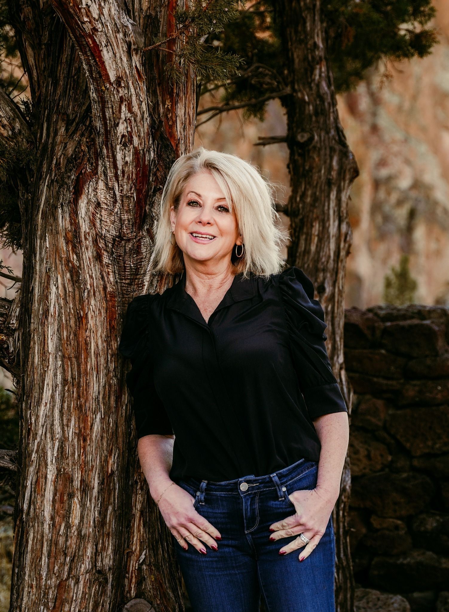 A woman in a black shirt and jeans is standing next to a tree.