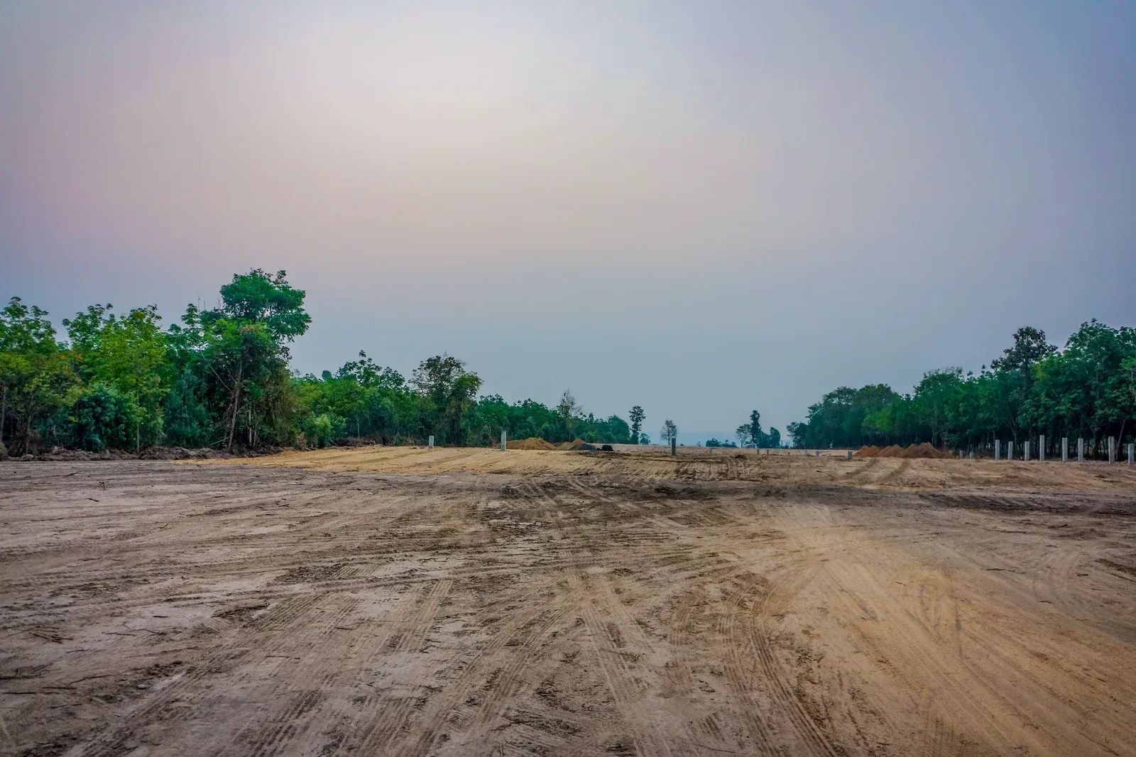 Dirt path leading toward a line of trees under a hazy sky.