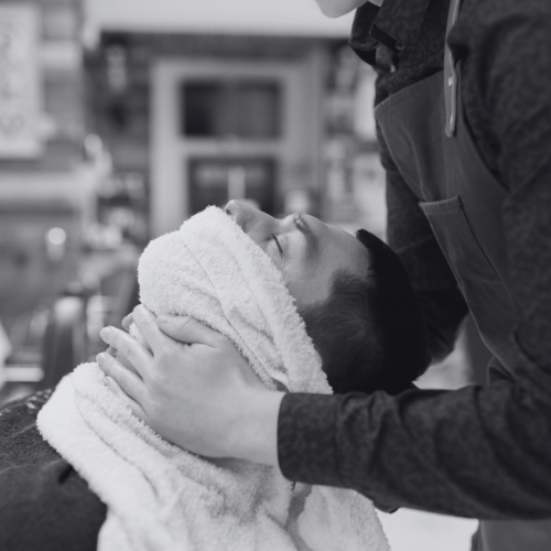 A black and white photo of a man getting his hair shaved by a barber