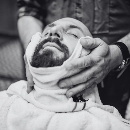 A man with a beard is getting a shave with a towel around his neck.
