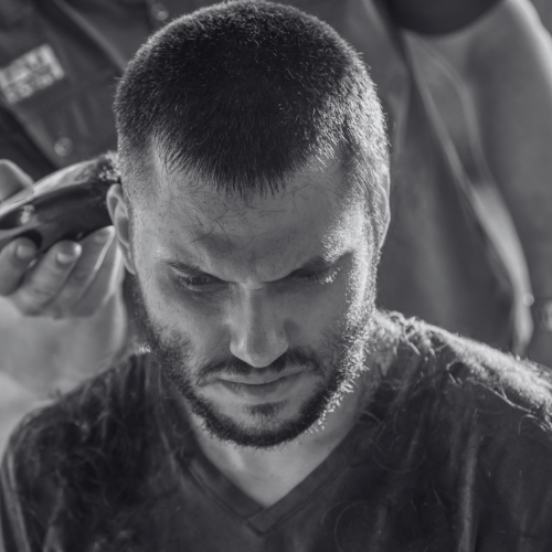 A man with a beard is getting his hair cut with a clipper.