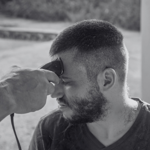 A man with a beard is getting his hair cut with a clipper.