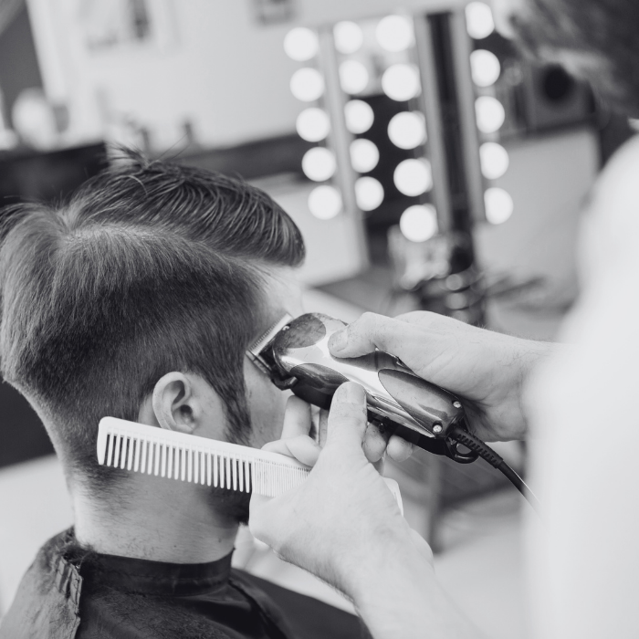 A man is getting his hair cut by a barber in a black and white photo.