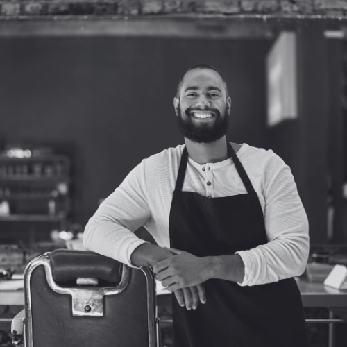A black and white photo of a man leaning on a barber chair