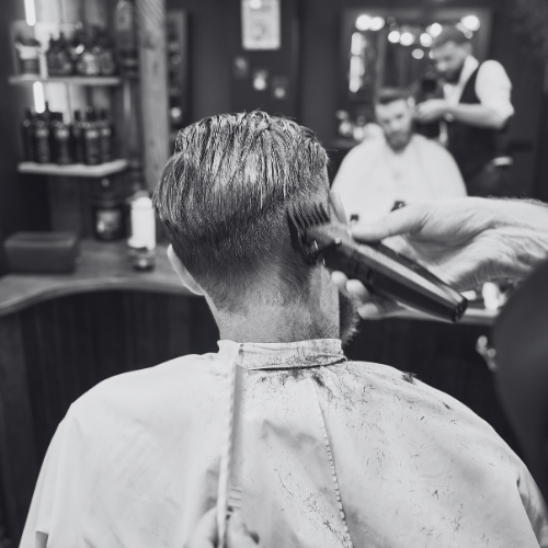 A man is getting his hair cut by a barber in a black and white photo.