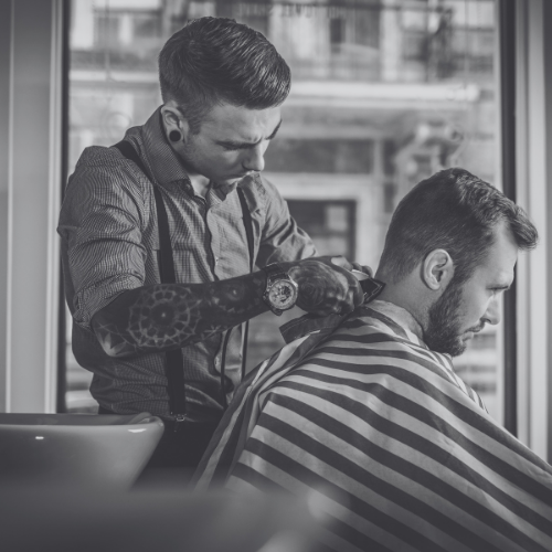 A man is getting his hair cut by a barber in a black and white photo.