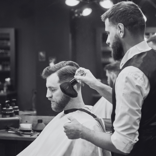A man is getting his hair cut by a barber in a black and white photo.