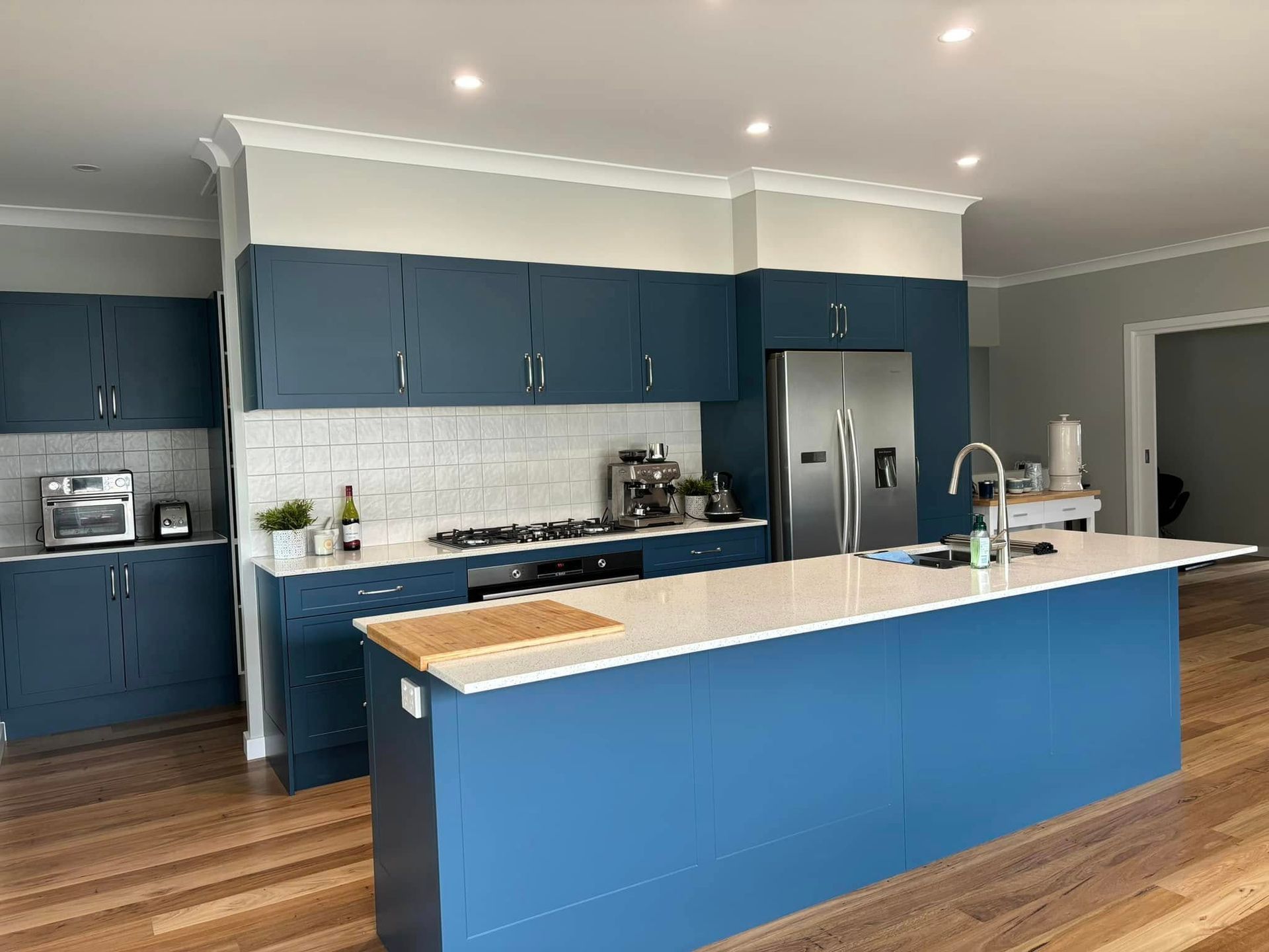 Modern white kitchen with a quartz countertop island, under-cabinet lighting, and light green walls — JRB Joinery In Kew, NSW