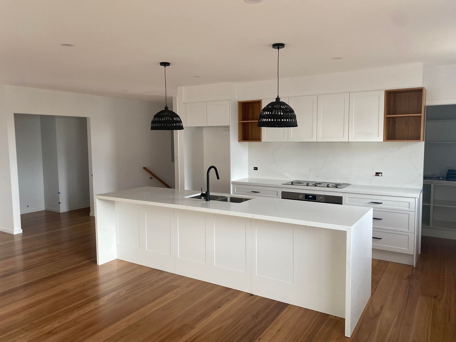 Modern white kitchen with island, black pendant lights, and hardwood floors.