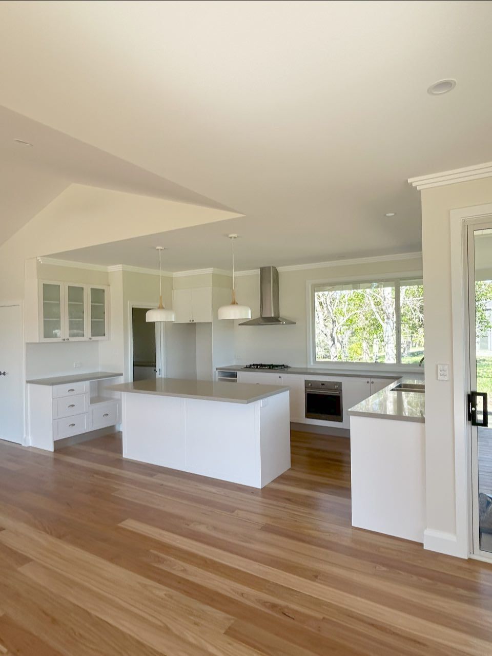 Modern white kitchen with island, stainless steel range hood, and light wood flooring.
