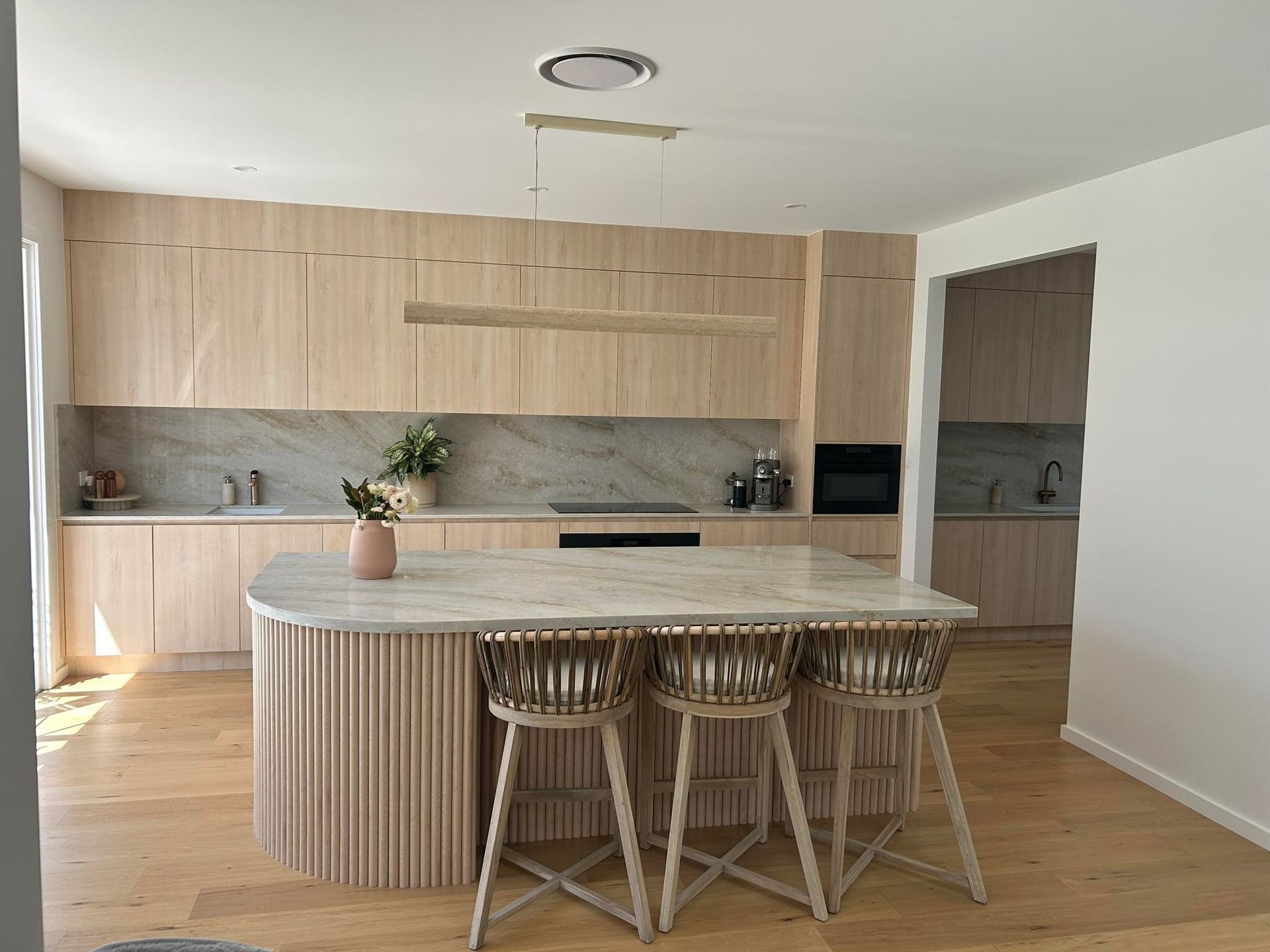 Modern kitchen with light wood cabinets, marble countertops, and island with stools.