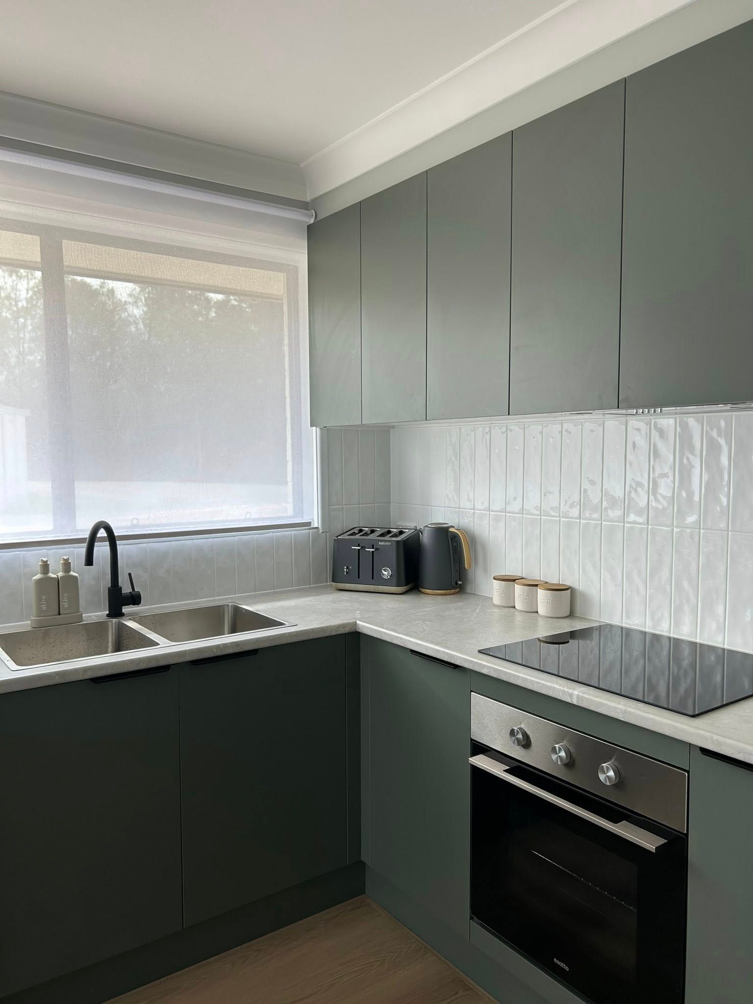 Green kitchen cabinets with white countertops, sink, and oven. A toaster sits on the counter.