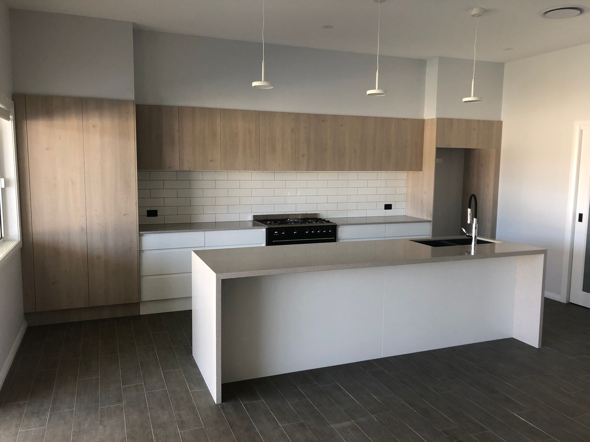 A modern kitchen with light wood upper cabinets, white lower cabinets, a white kitchen island, and white tile backsplash — JRB Joinery In Kew, NSW.