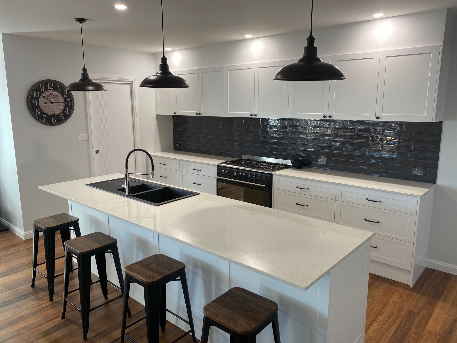 Modern kitchen with white cabinets, a large island featuring a black sink and stools, and a dark subway tile backsplash.
