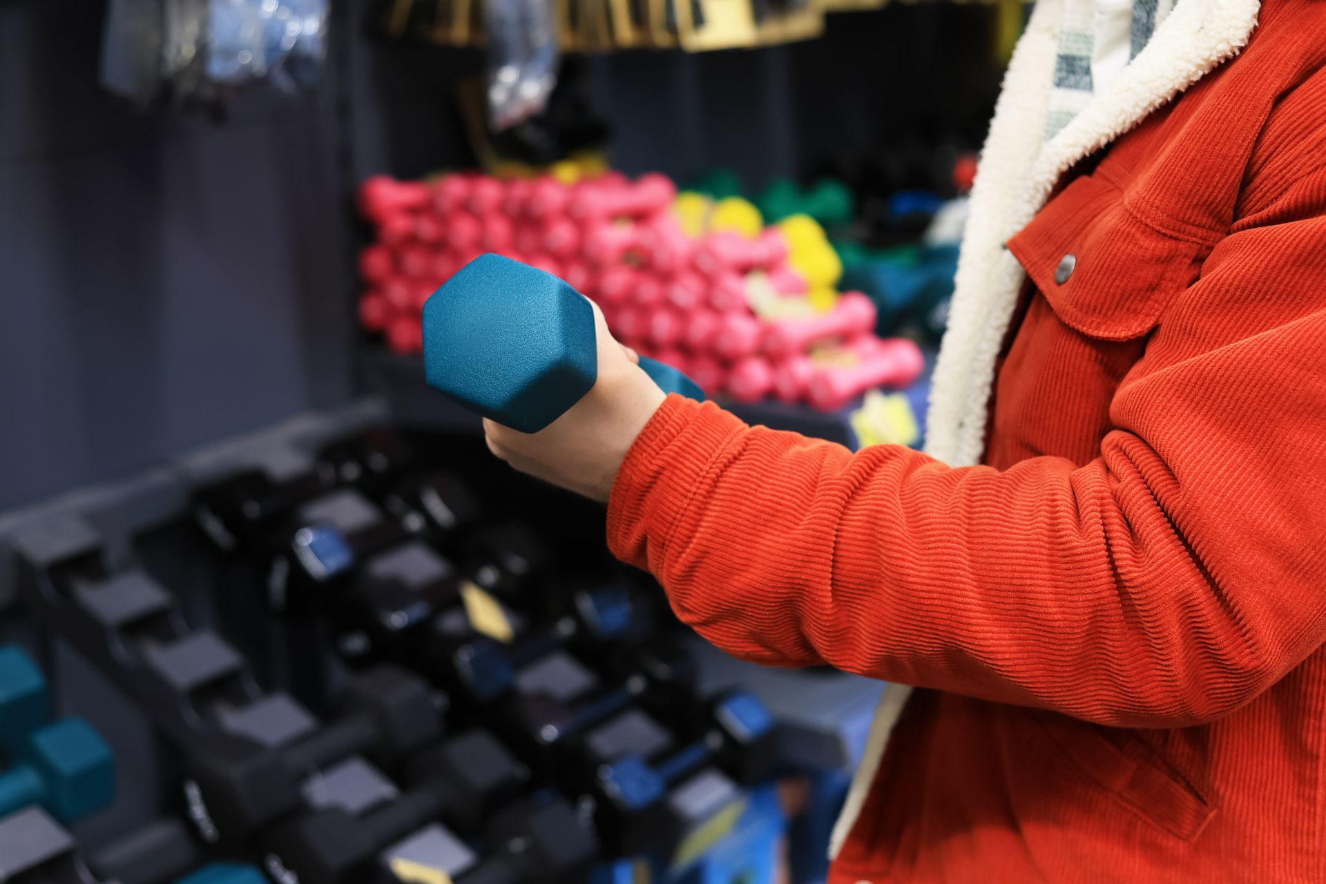 A man in a red jacket choosing a blue dumbbell in an exercise equipment showroom. A man in a red jacket choosing a blue dumbbell in an exercise equipment showroom.